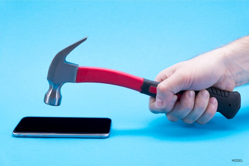 Close-up image of man hitting a cell phone with a hammer.